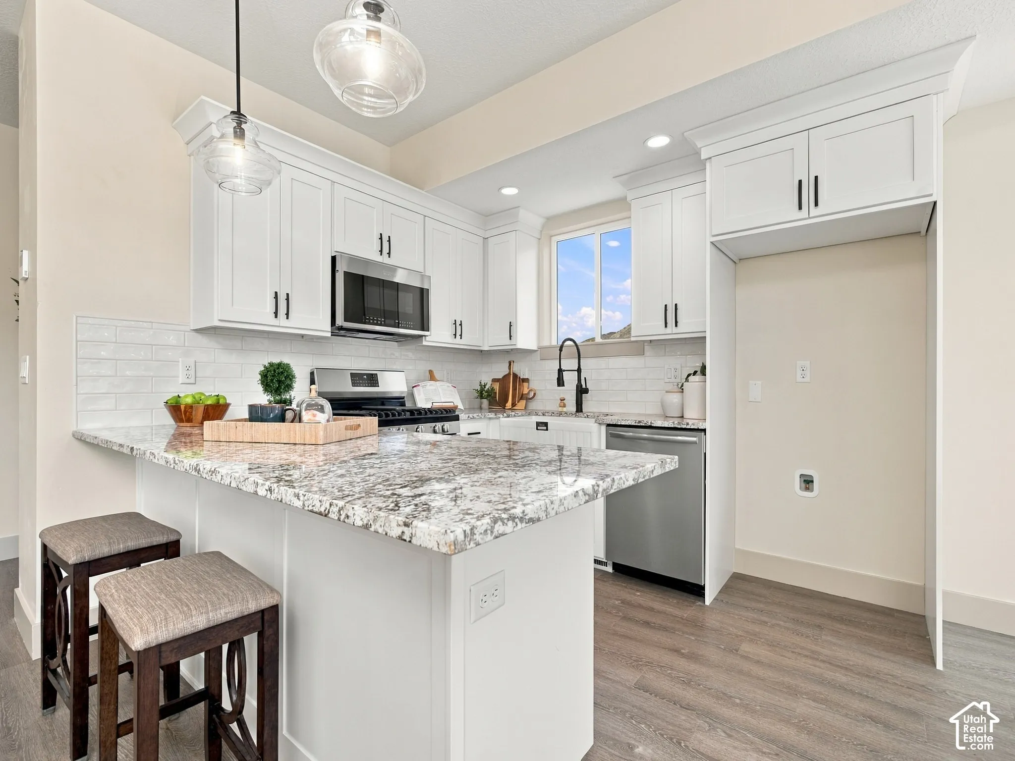 Kitchen featuring white cabinetry, light-toned countertops, stainless steel appliances, a subway tile backsplash, and wood-finish flooring