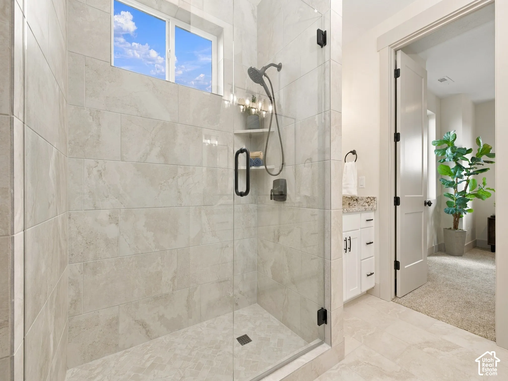 Glass-enclosed shower with a transom window, featuring light-toned tile surrounds and a built-in shower niche