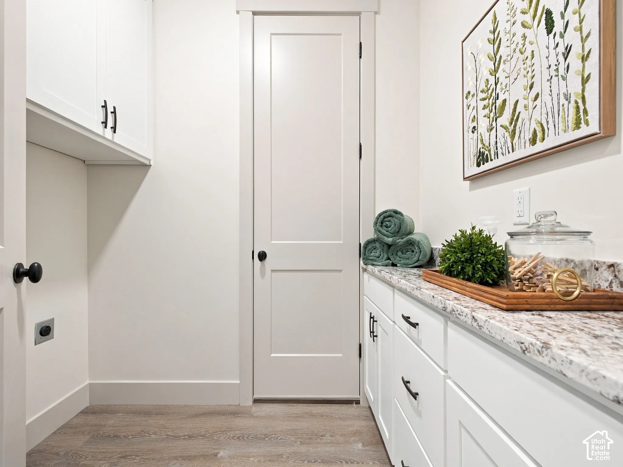 Elegant laundry room featuring white shaker-style cabinetry with oil-rubbed bronze hardware, marble-look countertops, and wood-finish flooring