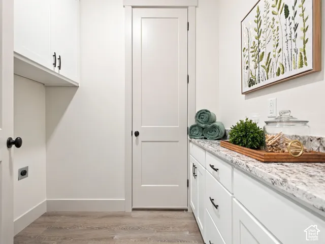 Elegant laundry room featuring white shaker-style cabinetry with oil-rubbed bronze hardware, marble-look countertops, and wood-finish flooring