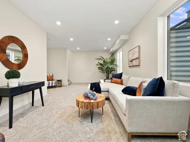 Expansive living space featuring recessed lighting, a large window with privacy blinds, and light-toned carpeting