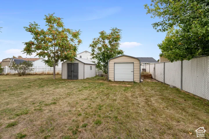 Expansive yard featuring two storage sheds, a chain-link fence, and mature trees