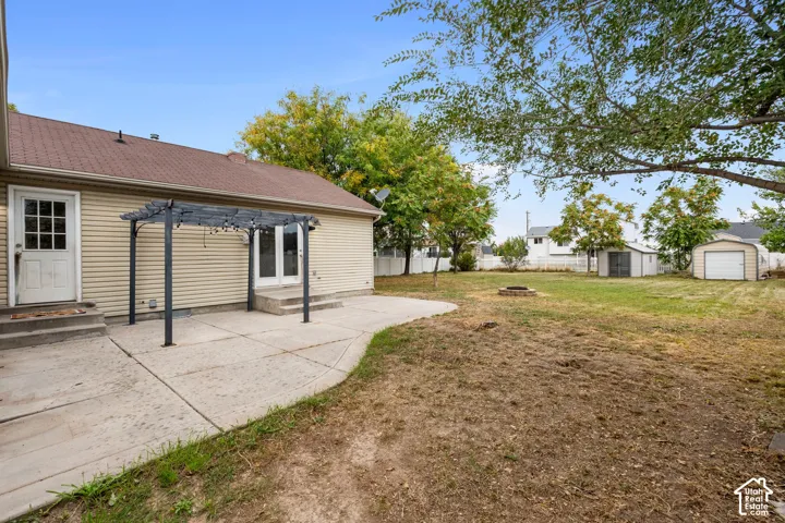Spacious 1/3 Acre backyard featuring a concrete patio, dual exterior access, and a freestanding pergola with fire pit