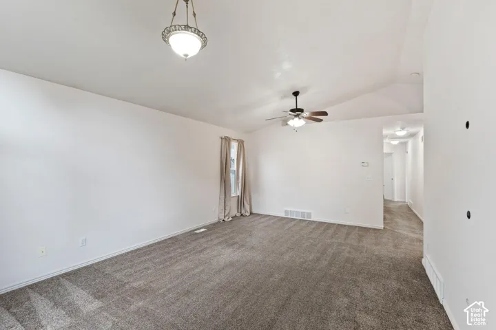 Vaulted ceiling with a ceiling fan, neutral wall paint, and gray carpet flooring