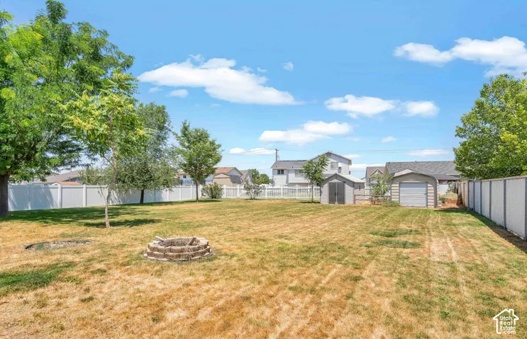 1/3 Acre Expansive yard featuring a built-in fire pit, mature trees, white vinyl fencing, a detached storage shed, and a detached garage with a roll-up door