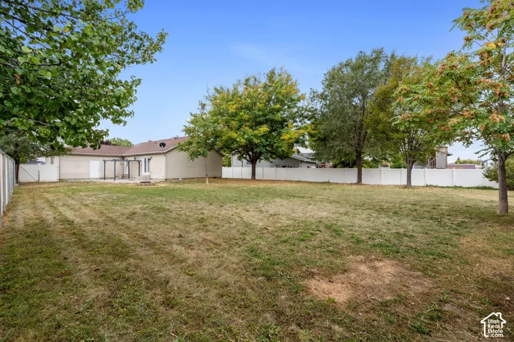 Expansive rear yard featuring a privacy fence, mature trees, and a concrete patio with a pergola