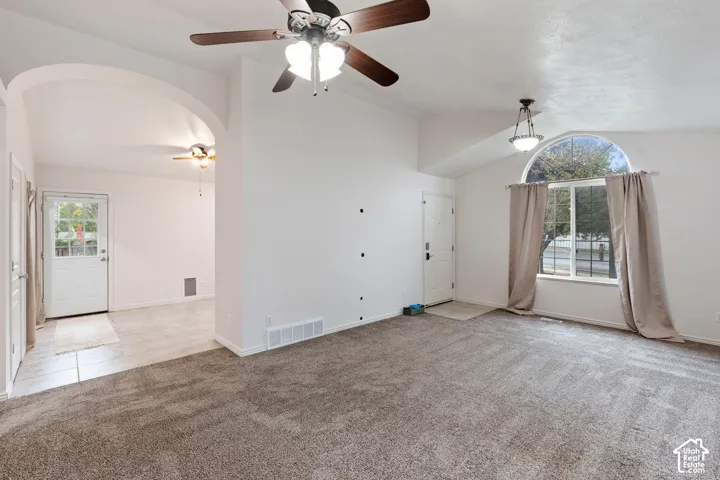 Vaulted ceiling with an arched window, ceiling fan, carpet flooring, recessed entry, and tile flooring