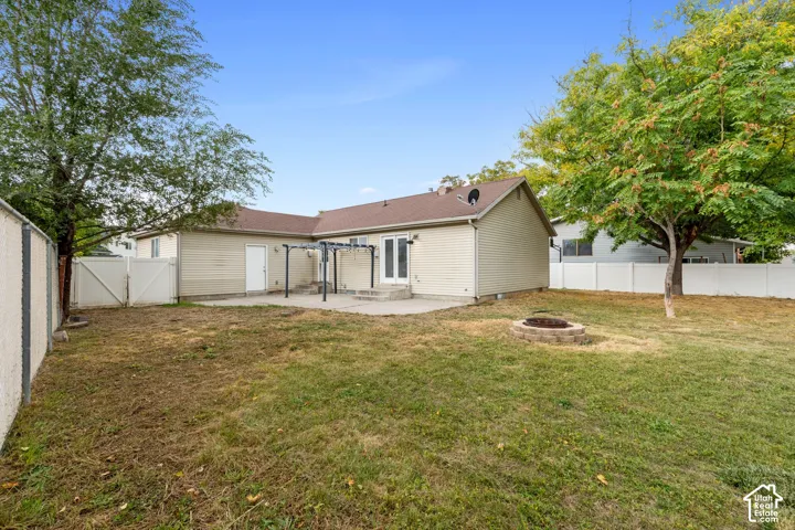Spacious 1/3 Acre backyard featuring a stone-finish fire pit, concrete patio, pergola structure, and mature trees
