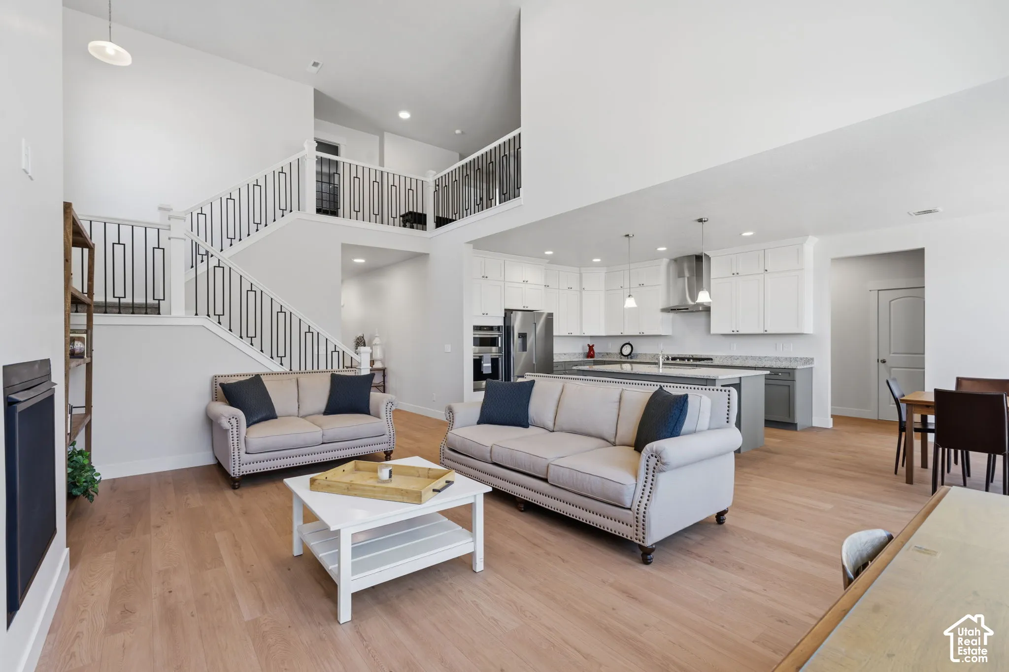 Open-concept living space featuring soaring ceilings, a mezzanine-level loft with metal railings, and abundant natural light from recessed ceiling fixtures.