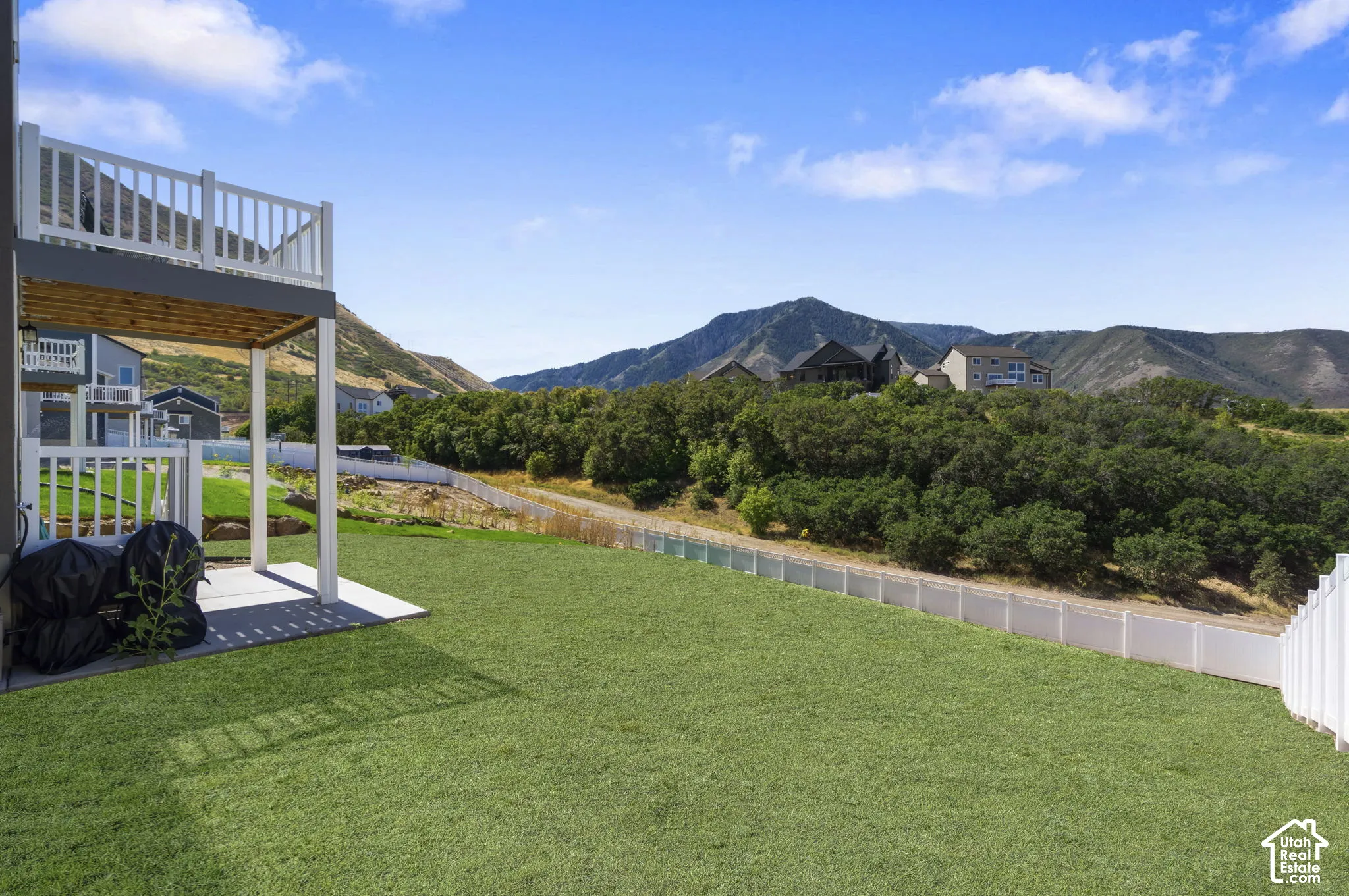 **AI GRASS**expansive grassy yard with mountain backdrop, featuring a lower-level concrete patio and an upper-level deck with white railings.