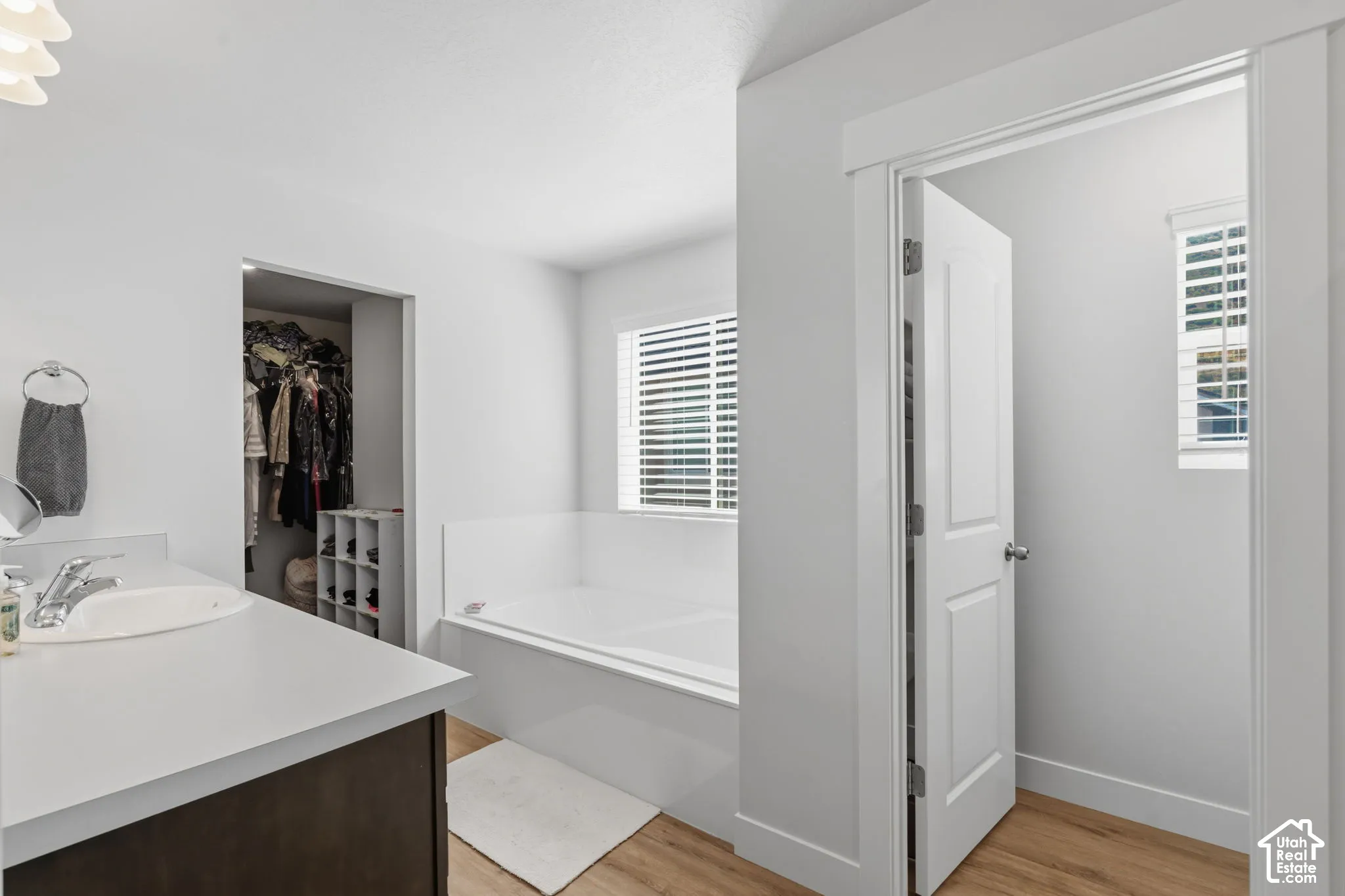 Master bath with soaking tub, LVP flooring, vanity with white countertop, built-in open shelving in closet, and white interior doors.