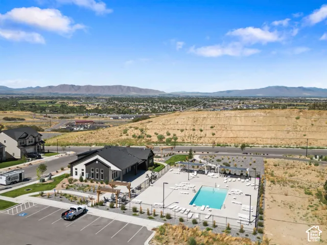 Resort-style pool with surrounding lounge areas, modern clubhouse building, expansive hardscaping, and mountain backdrop.