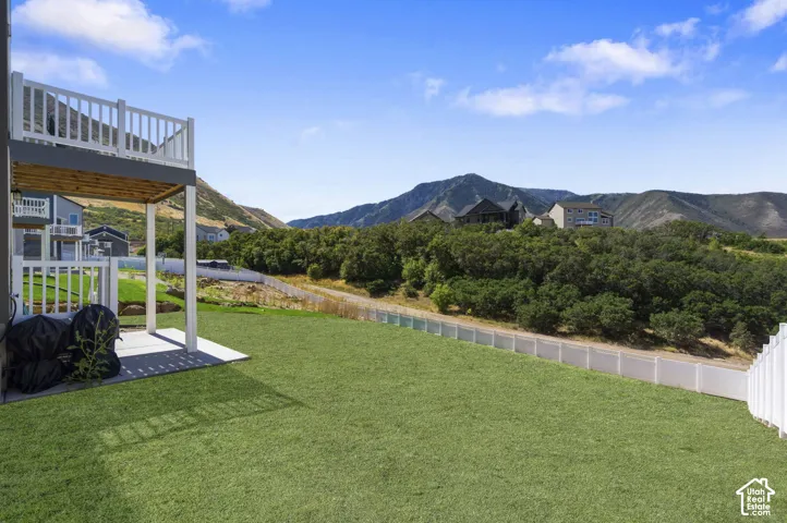 **AI GRASS**expansive grassy yard with mountain backdrop, featuring a lower-level concrete patio and an upper-level deck with white railings.