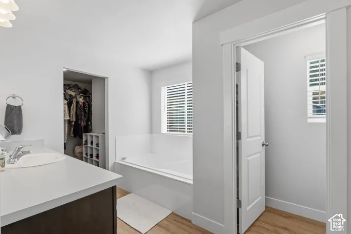 Master bath with soaking tub, LVP flooring, vanity with white countertop, built-in open shelving in closet, and white interior doors.