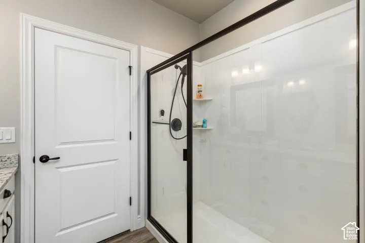 White paneled door with black hardware, granite-look countertop, wood-finish flooring, glass-enclosed shower with black trim, and shower-mounted shelving