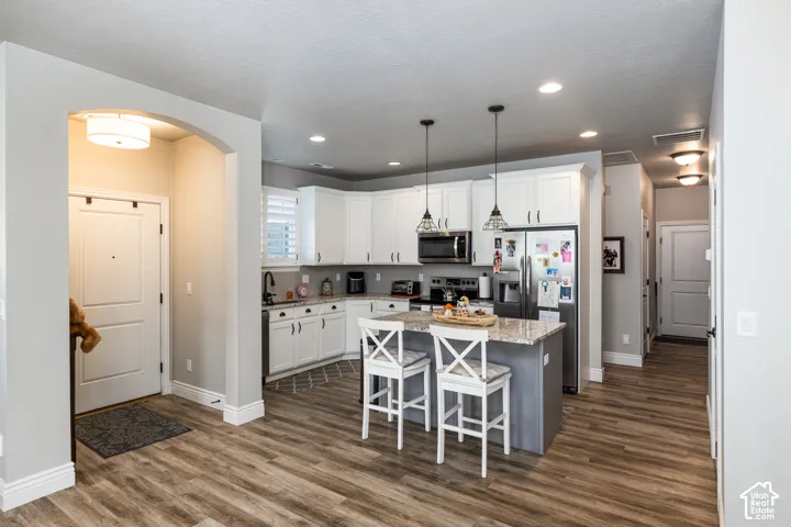 Open-concept kitchen featuring white cabinetry, stainless steel appliances, a center island with pendant lighting, and wood-finish flooring