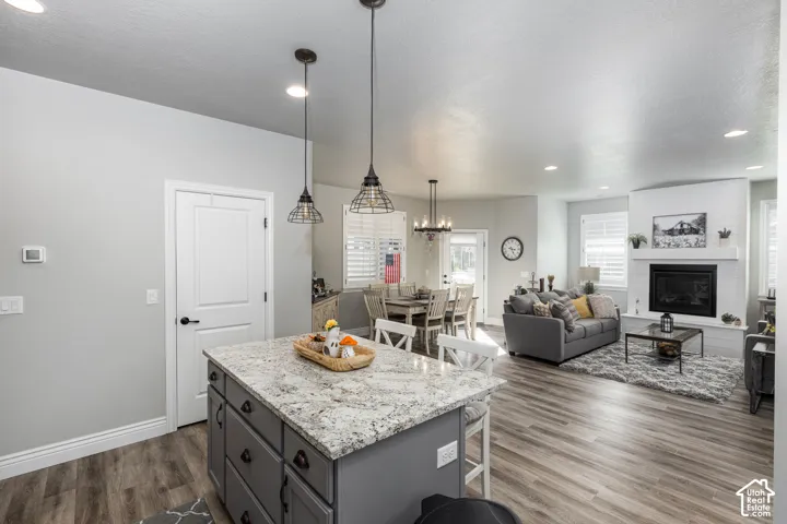 Kitchen island with granite countertop, wood-finish flooring, recessed lighting, white fireplace with shiplap accent, and louvered window treatments
