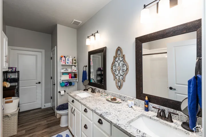 Dual vanity with undermount sinks, granite-look countertop, white cabinetry, and wood-finish flooring