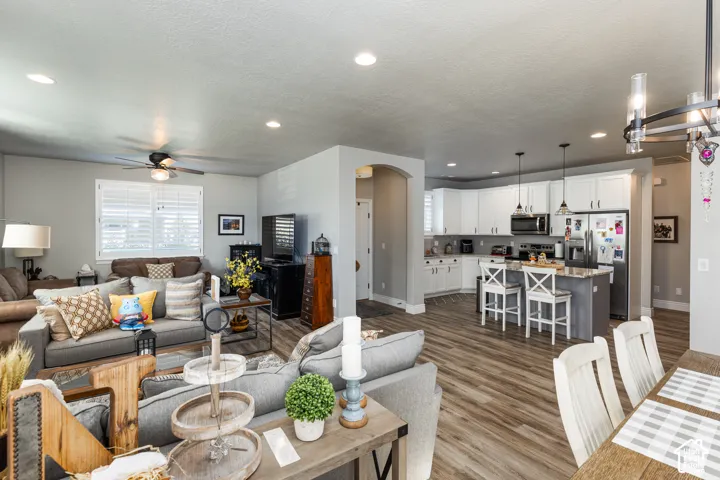 Open-concept living space featuring wood-finish flooring, recessed lighting, white cabinetry, a kitchen island with seating, and stainless steel appliances