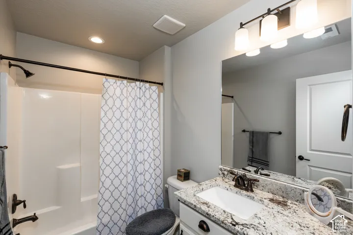 Bathroom featuring a white vanity with a light-colored countertop, an integrated rectangular sink, a mirrored wall, and a bathtub with a shower fixture