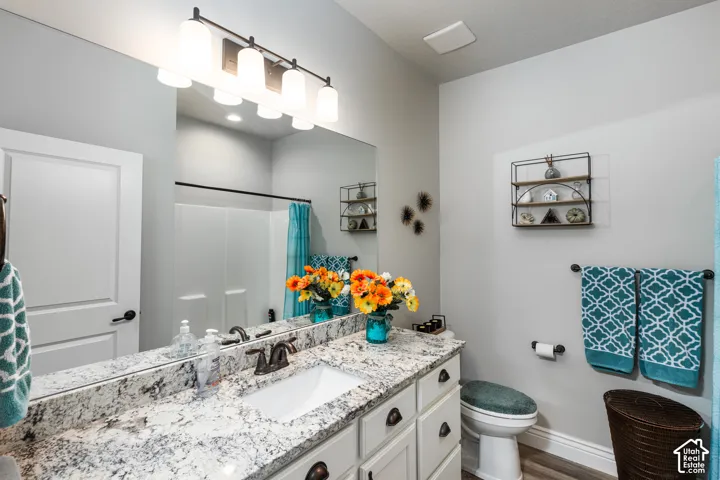 Bathroom featuring a vanity with an undermount sink, a granite-finish countertop, a large mirror, and wood-finish flooring