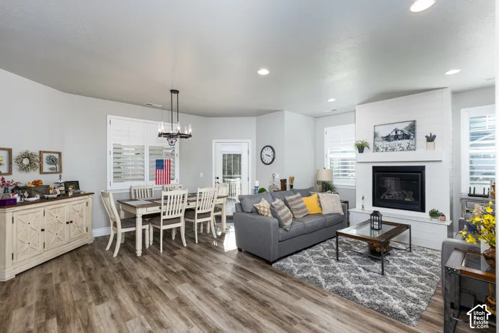 Open-concept living area with wood-finish flooring, recessed lighting, a fireplace featuring a shiplap surround, and white plantation shutters on multiple windows