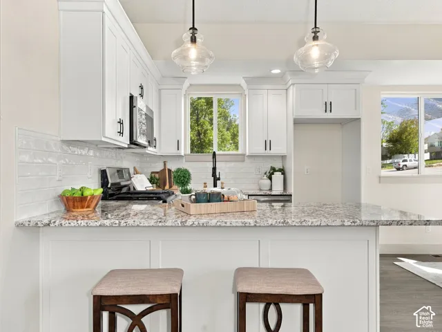 Kitchen featuring white shaker-style cabinetry, granite countertops, subway tile backsplash, and two pendant light fixtures