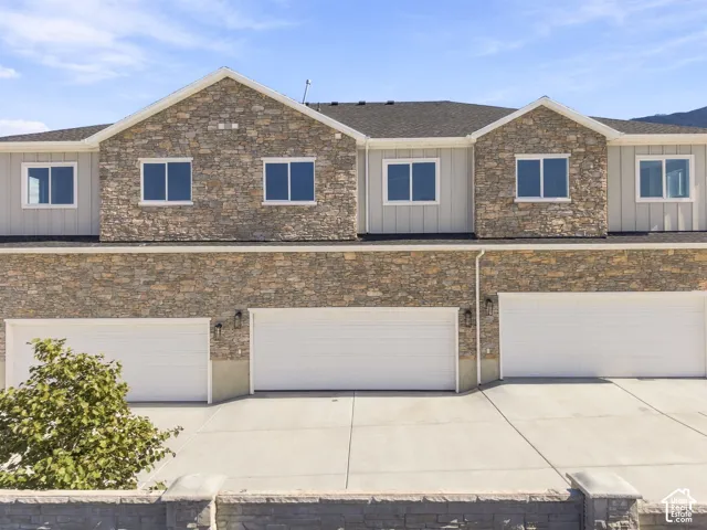 Stone facade, multiple garage doors, concrete driveway, light siding accents, dark shingle roof
