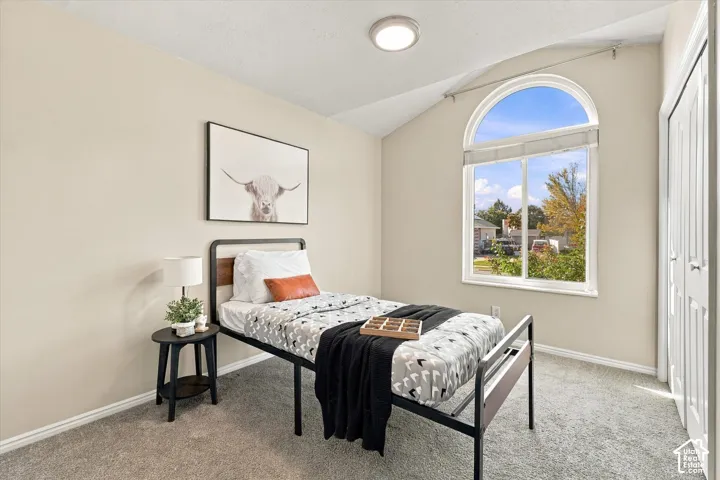 Bright secondary bedroom showcasing arched transom window with natural light, carpeted flooring, black metal bed frame, neutral wall finishes, and recessed ceiling lighting