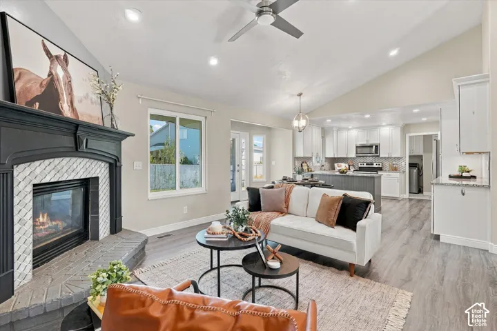 Vaulted ceiling, fireplace with tile surround, wood-finish flooring, recessed lighting, and a ceiling fan