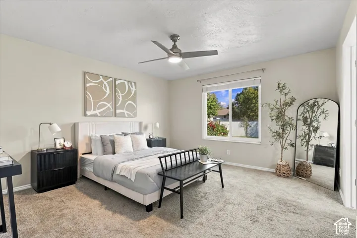 Neutral-toned wall paint, ceiling fan with integrated lighting, window with exterior landscape, light-colored carpeting, and a framed bed