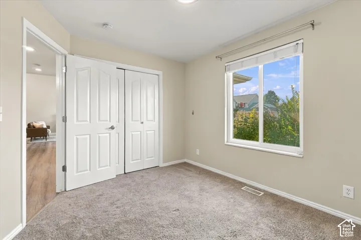 Bright bedroom featuring neutral carpeting, dual closets with white six-panel doors, large window with natural light, and smooth ceiling with recessed lighting