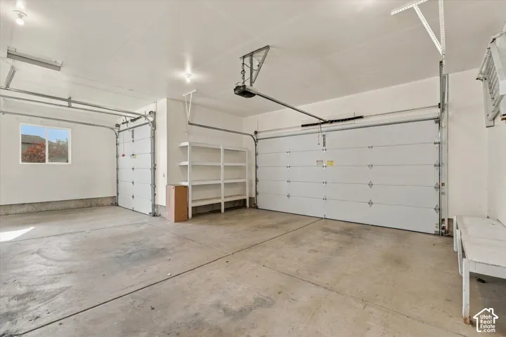 Spacious three-car garage with epoxy-coated concrete flooring, overhead storage shelving, and multiple garage door openers