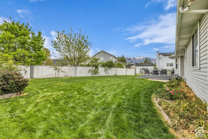 Expansive backyard featuring a meticulously manicured lawn, mature landscaping with established trees and shrubs, white vinyl privacy fencing, and a patio area with outdoor seating space
