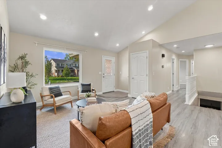 Vaulted ceiling with recessed lighting, light-toned walls, wood-finish flooring, white trim, and a white interior door