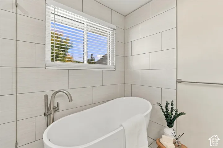 Freestanding soaking tub with a floor-mounted brushed nickel faucet, large format rectangular wall tiles, and a window with blinds