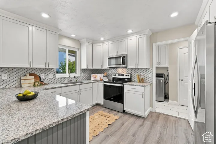 Modern kitchen featuring white cabinetry with brushed nickel hardware, granite-style countertops, geometric tile backsplash, stainless steel appliances including a gas range and built-in microwave, and wood-finish flooring throughout the open layout