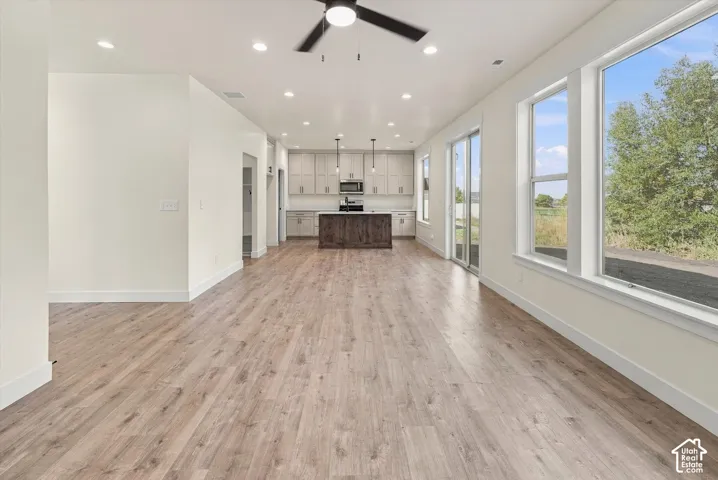 Open-concept living space featuring wood-finish flooring throughout, abundant natural light from expansive windows, vaulted ceiling with recessed lighting and ceiling fan, and a modern kitchen with stainless steel appliances and island cabinetry