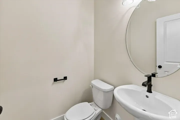 Pedestal sink with a matte black faucet, wall-mounted circular mirror, and overhead vanity lighting