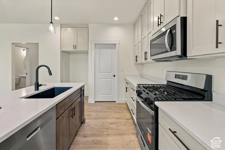 White shaker-style cabinetry with matte black hardware, stainless steel appliances, a black basin sink with matte black faucet, light-toned wood-finish flooring, and white countertops