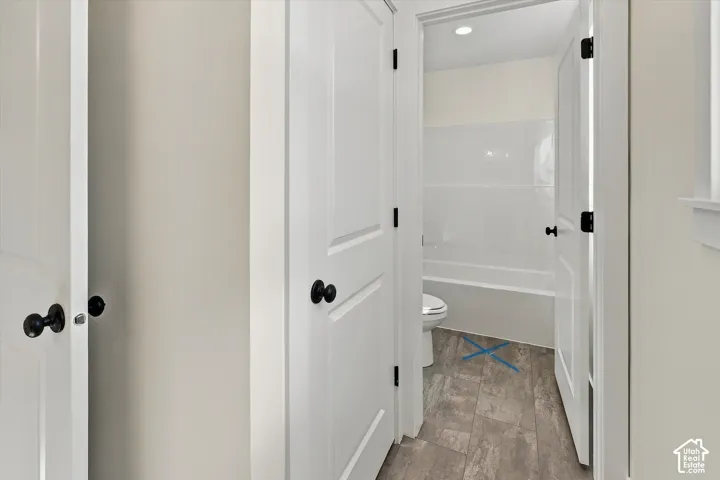 Bright hallway with white six-panel doors featuring matte black hardware, neutral wall finishes, and wood-finish flooring throughout the corridor space