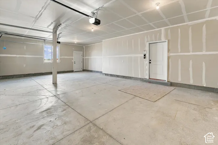 Spacious garage featuring polished concrete flooring, recessed ceiling lighting, overhead garage door with automatic opener, and dual white panel entry doors
