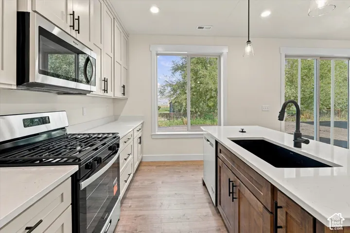 Modern galley kitchen featuring white cabinetry with brushed metal hardware, quartz countertops, a gas cooktop with stainless steel range hood, and a black undermount sink with matte black faucet