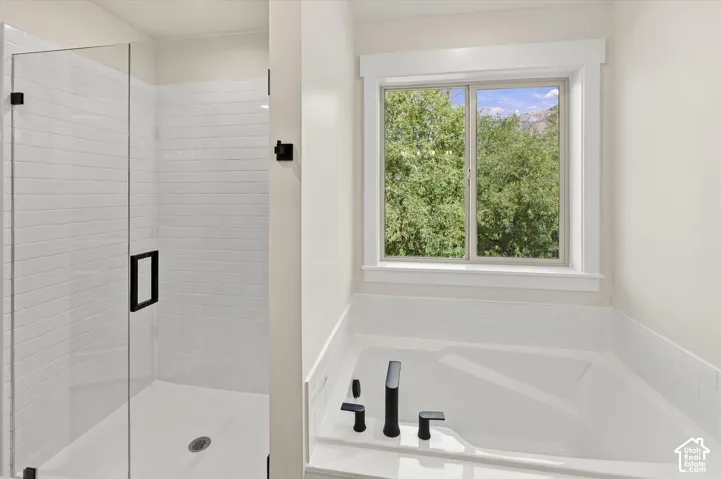 Glass-enclosed shower with subway tile surround, matte black hardware, built-in soaking tub with matte black fixtures, and a window with white trim