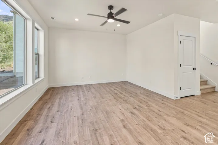 Spacious room featuring wood-finish flooring, ample natural light from large windows, recessed lighting, and a ceiling fan