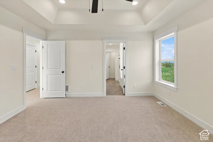 Tray ceiling with recessed lighting and a ceiling fan, white trim work, light-colored carpeting, and a window with a white frame