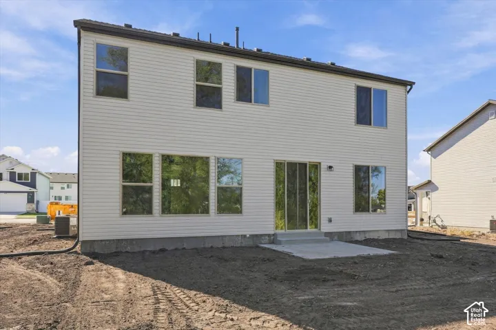 White vinyl siding exterior with multiple windows, concrete foundation, rear concrete patio, and sliding glass door