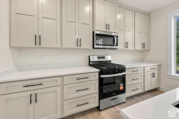 Light-toned shaker cabinetry with matte black hardware, stainless steel gas range, over-the-range microwave, light quartz countertops, and wood-finish flooring