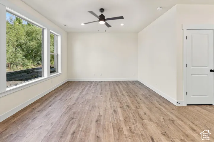 Spacious room with wood-finish flooring, multiple windows, a ceiling fan with integrated lighting, and recessed lighting