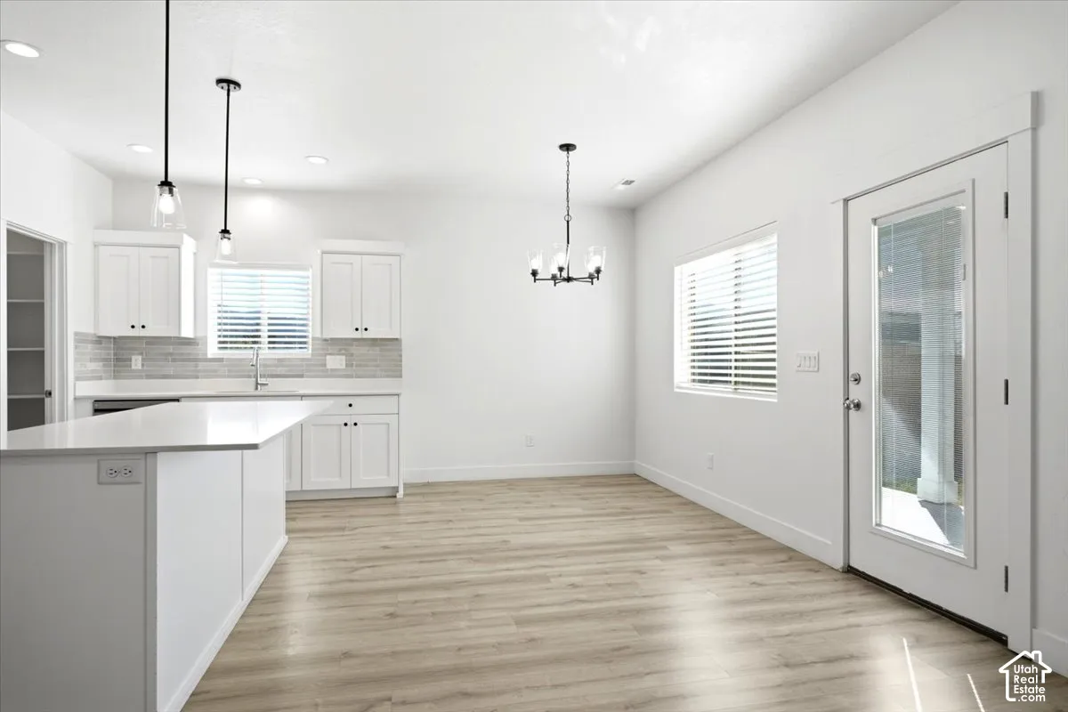 Kitchen featuring white cabinetry with dark hardware, a white island with an integrated sink, and wood-finish flooring